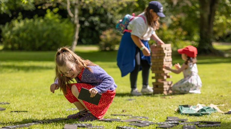 Children play with a giant dominos set on a green lawn in the sunshine.